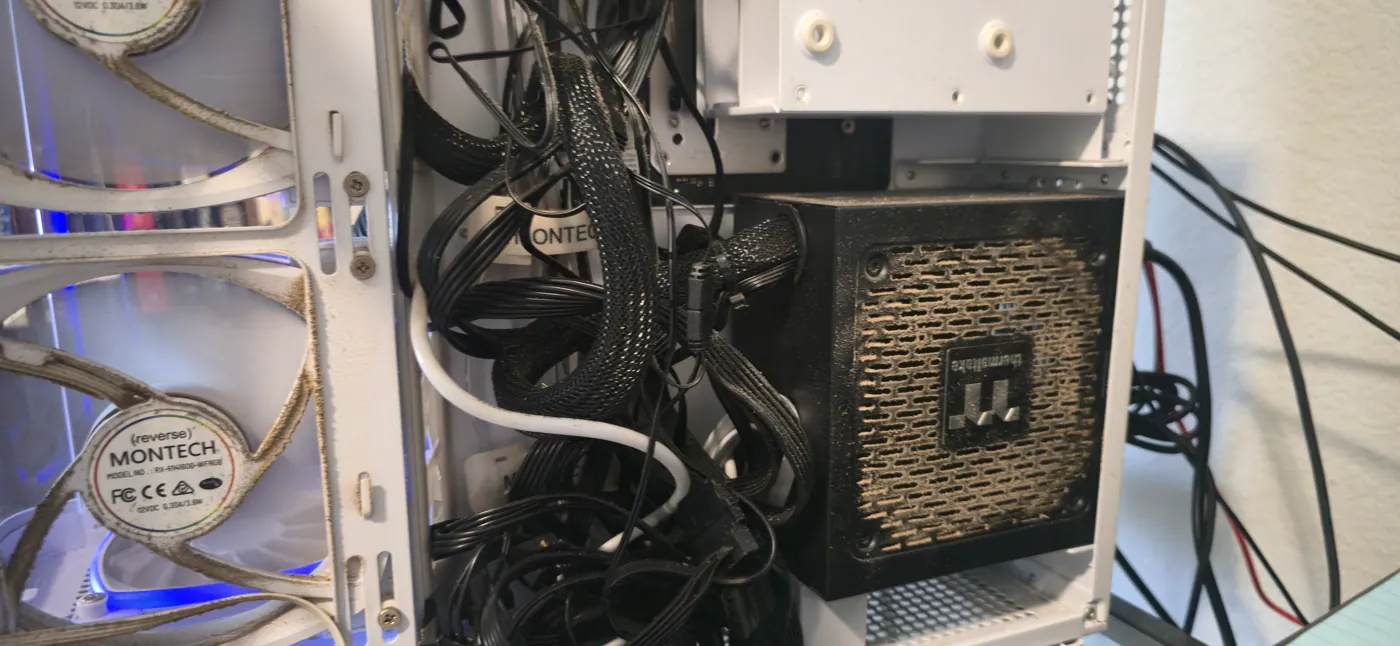 Inside the case mid-build — power supply, sleeved cabling, and a case fan, lit faint blue.